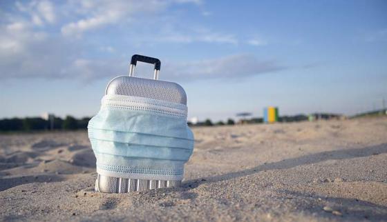 Koffert på strand med munnbind rundt.